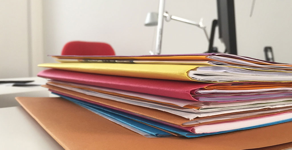 Vue de dessus d'un dossier kraft ouvert contenant des documents administratifs français bien organisés avec intercalaires colorés, entouré d'un stylo, de trombones dorés et d'un petit cactus, sur une surface en bois clair.